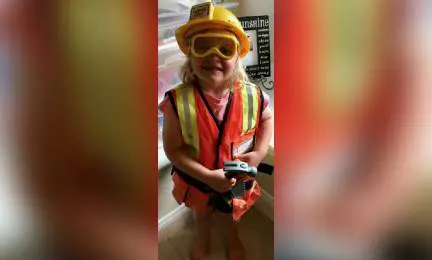 A little girl in an orange vest and hard hat.