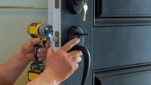 A person is installing a bedroom doorknob with lock and key using a power drill.