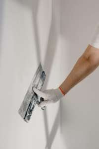 A person's arm holding a putty knife against a wall with shadows, repairing drywall.