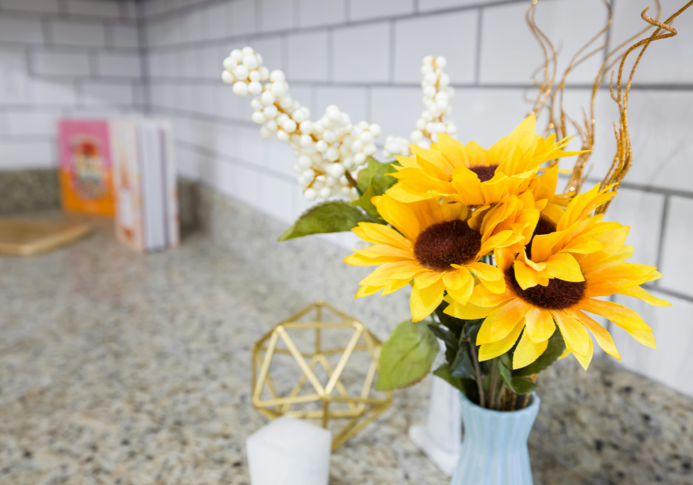 Artificial sunflowers in a blue vase on a kitchen countertop made of quartz, with decorative items in the background.